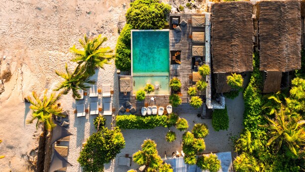 An aerial view of a beach resort with a swimming pool, lounge chairs, and palm trees.