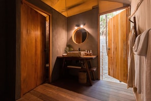 A wooden bathroom with a round mirror, wooden doors, and a sink with toiletries.