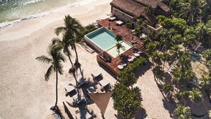 An aerial view of a beachside resort with a swimming pool, lounge chairs, and palm trees.