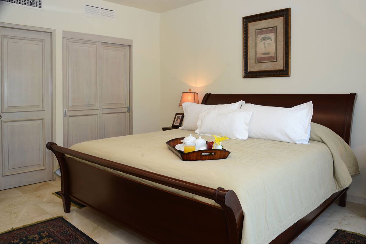 A neatly made bed with a tray of breakfast items, a framed picture on the wall, and a pair of closed doors.