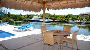 Un espacio al aire libre techado con piscina, sillones de descanso y una mesa con fruta.