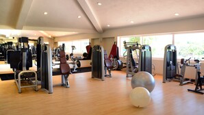 Un gimnasio con diferentes máquinas de ejercicio, un espejo y ventanas amplias.