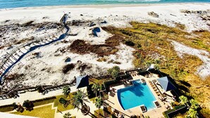 Ett flygbildsfoto av ett semesterområde med en swimmingpool, palmer och en strand.
