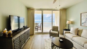 Ett hotellrum med en tv, en takfläkt, en balkong med utsikt över havet, en soffa och ett soffbord.