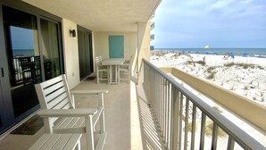 Ein Balkon mit Tisch und Stühlen, einer Tür und Blick auf einen Strand mit Sonnenschirmen und Menschen.