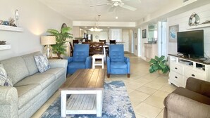 Ein geräumiges Wohnzimmer mit einer Couch, zwei blauen Sesseln, einem Couchtisch und einem Fernseher.