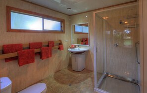 A bathroom with a shower, toilet, sink, and a towel rack with red towels. - Trade Winds Country Cottages (Norfolk Island)