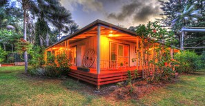 A cozy, single-story house with a porch, surrounded by lush greenery and palm trees. - Trade Winds Country Cottages (Norfolk Island)