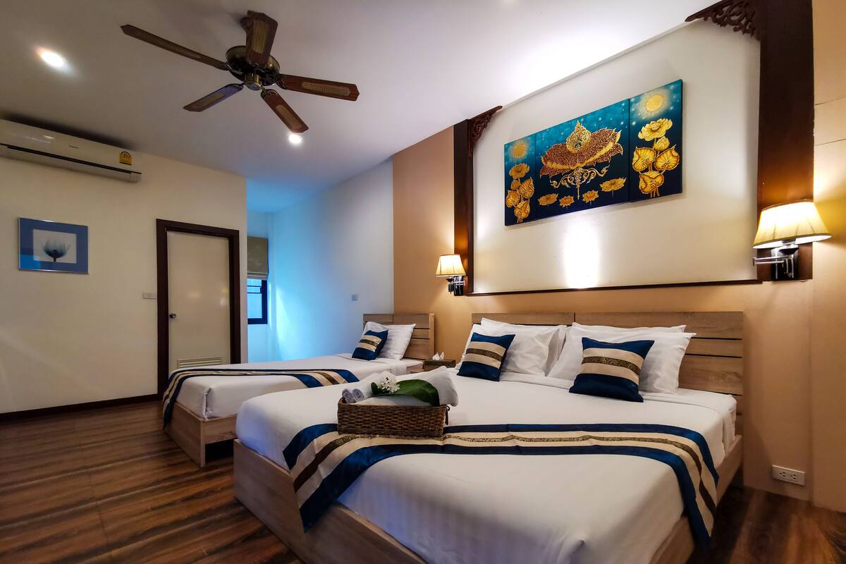 A hotel room with two beds, a ceiling fan, a wall-mounted artwork, and a nightstand with a lamp.