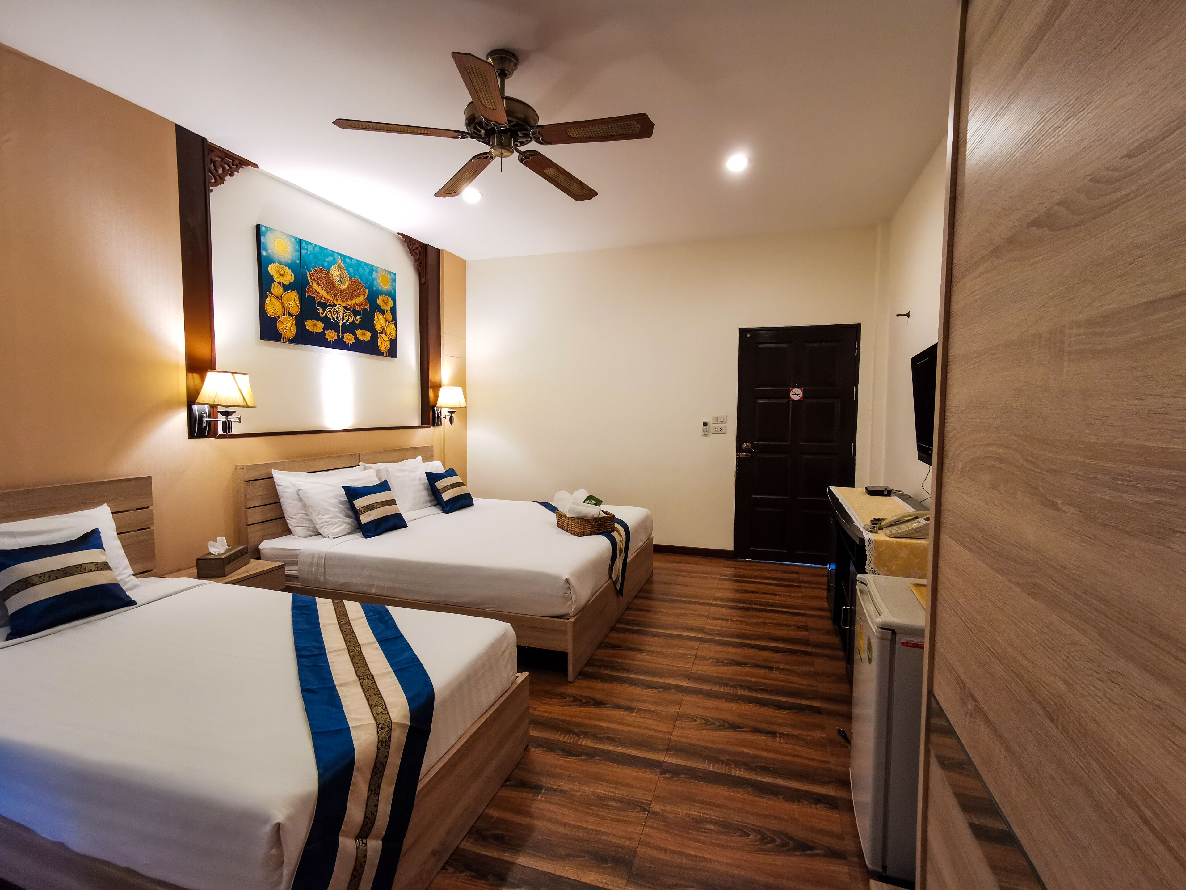 Une chambre d’hôtel avec deux lits, un ventilateur de plafond, un tableau, une télévision et un réfrigérateur.