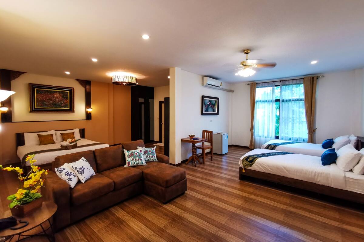 A hotel room with a large bed, a sofa, a desk, and a ceiling fan.