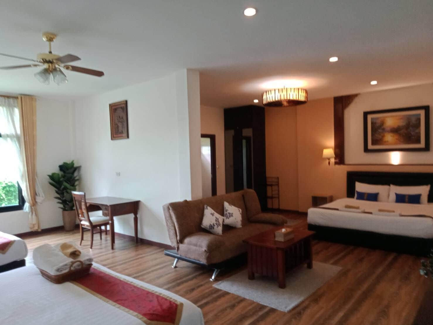 A hotel room with a bed, a sofa, a dining table, and a ceiling fan.