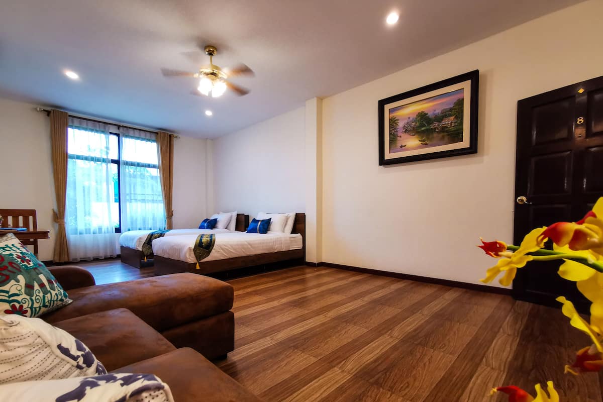 A hotel room with two beds, a brown sofa, a wooden floor, a ceiling fan, and a painting on the wall.