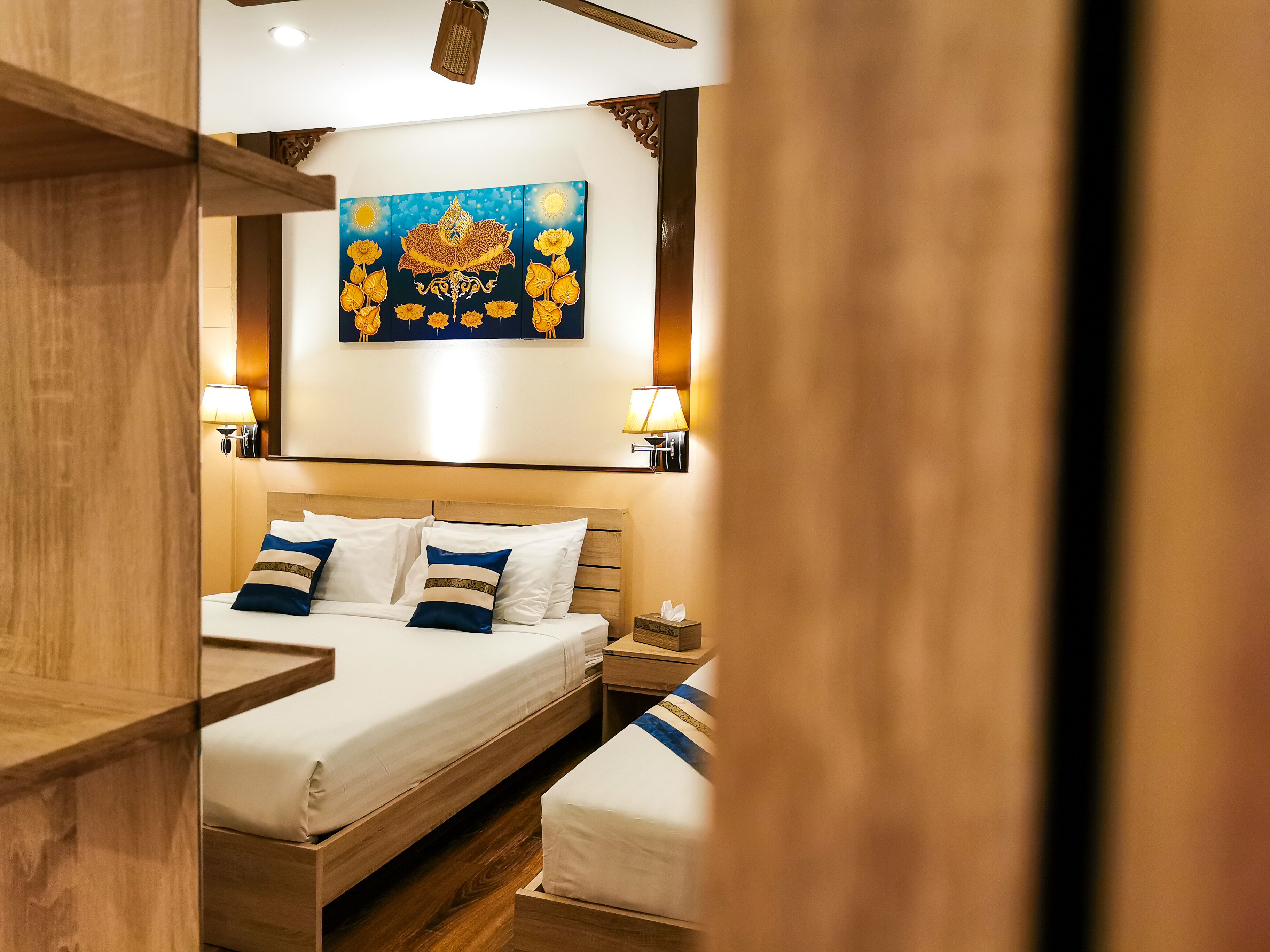 A hotel room with a wooden bed, a nightstand, a bedside table, and a wall-mounted painting.