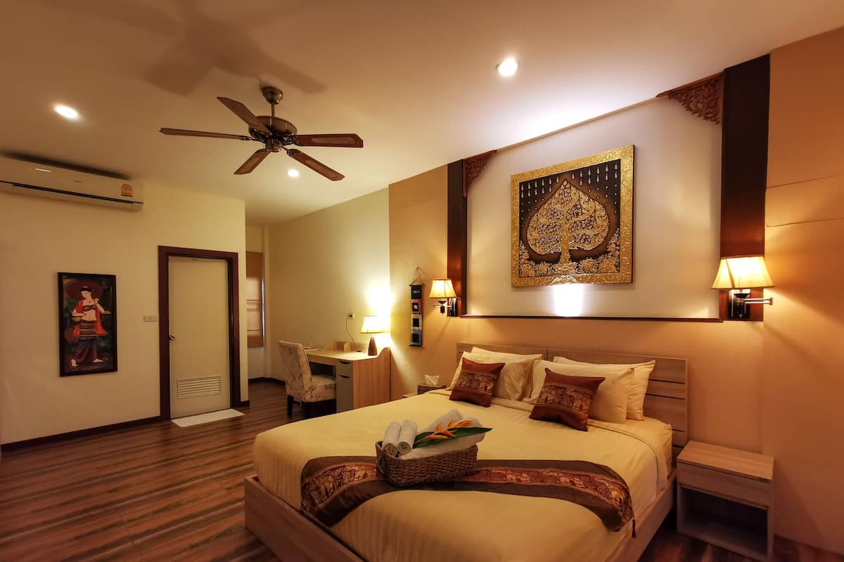 A hotel room with a large bed, a desk, a ceiling fan, and a wall-mounted lamp.