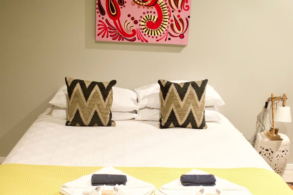 A neatly made bed with two pillows, a yellow blanket, and two folded towels.