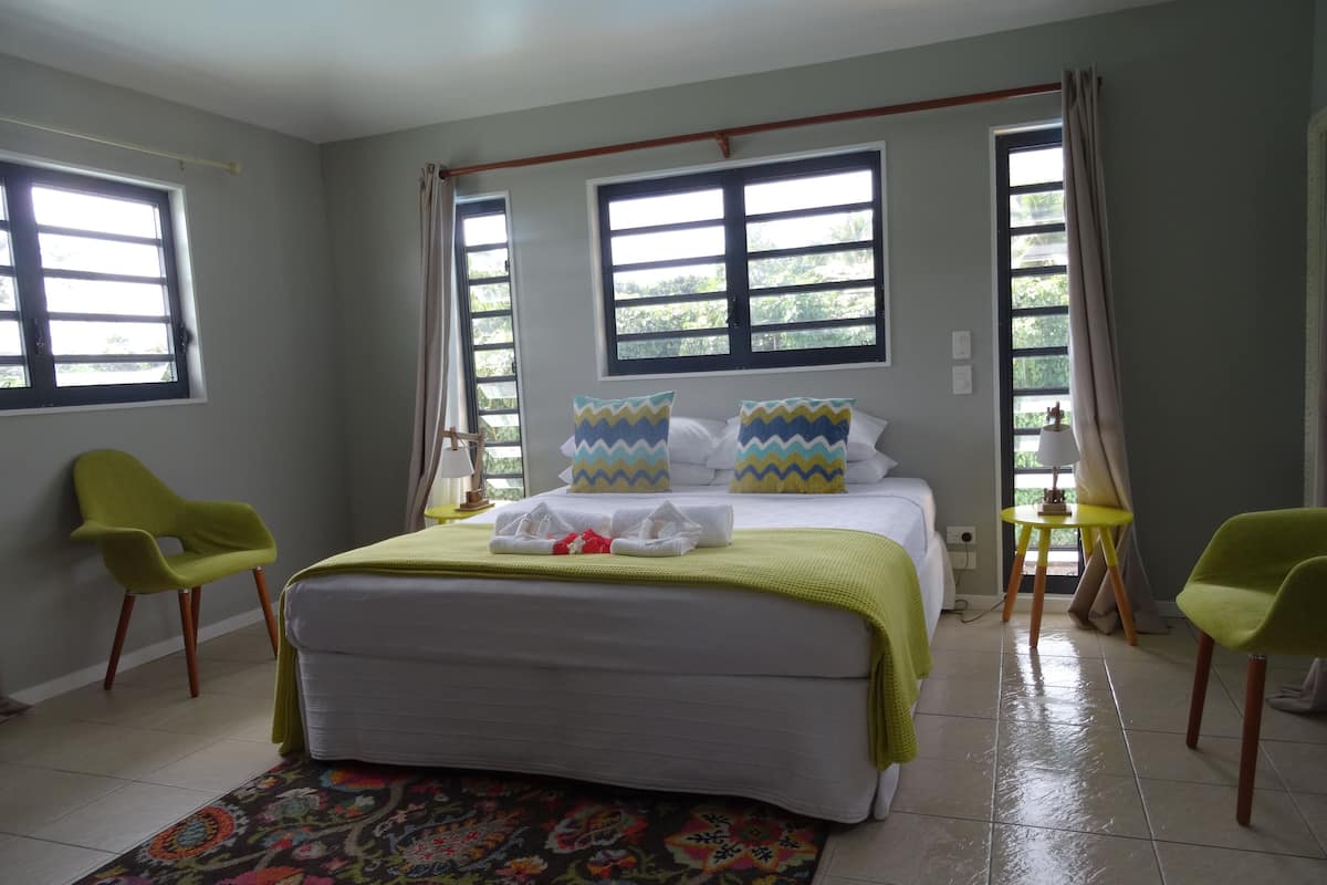 A bedroom with a bed, two chairs, a small table, and a window.