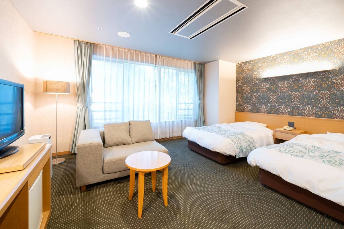 Une chambre d’hôtel avec un canapé, une petite table ronde, deux lits, une télévision et un mur décoré d’un motif.