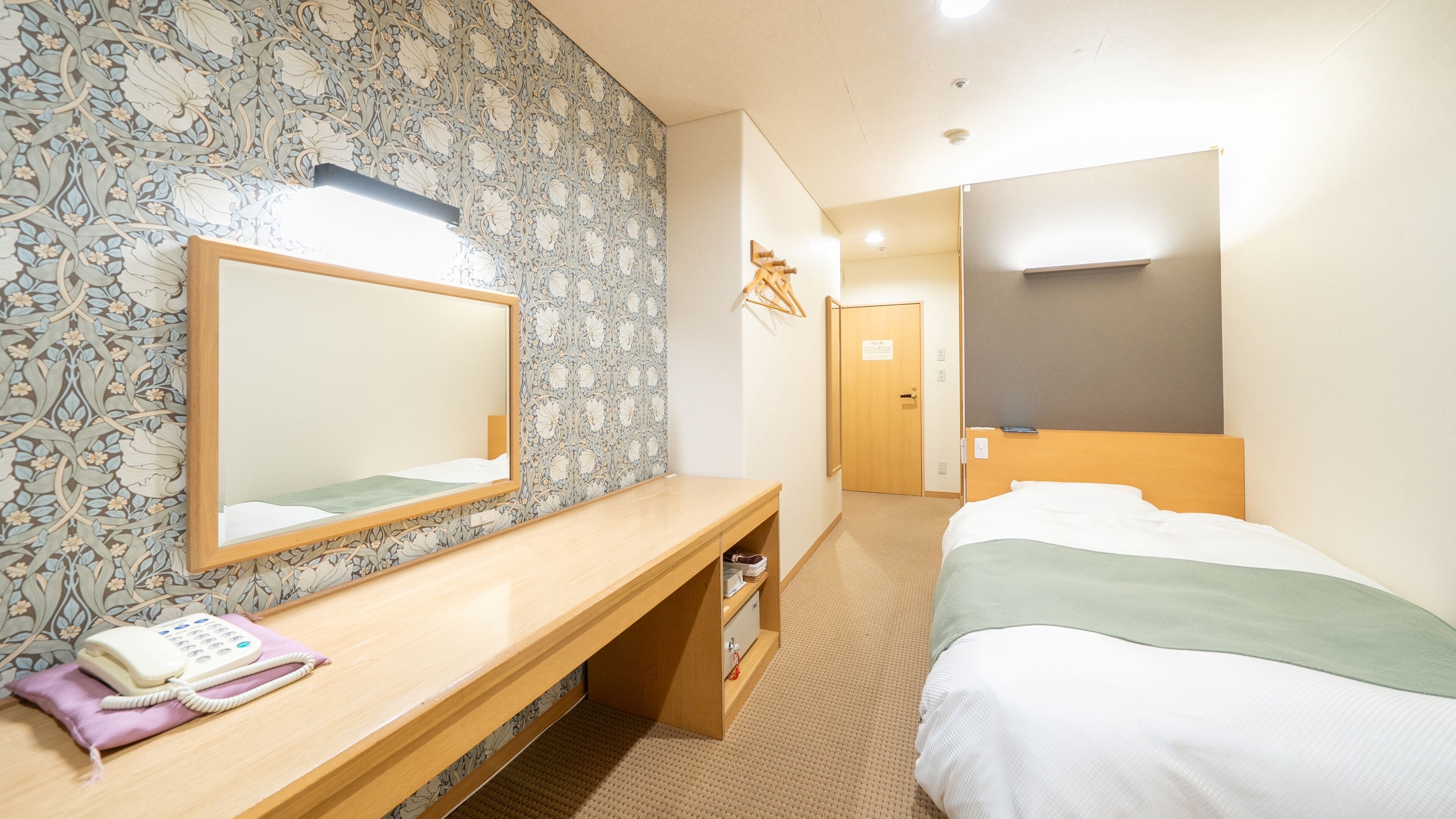 Une chambre d’hôtel avec un bureau en bois, un téléphone, un miroir, un lit et une armoire.