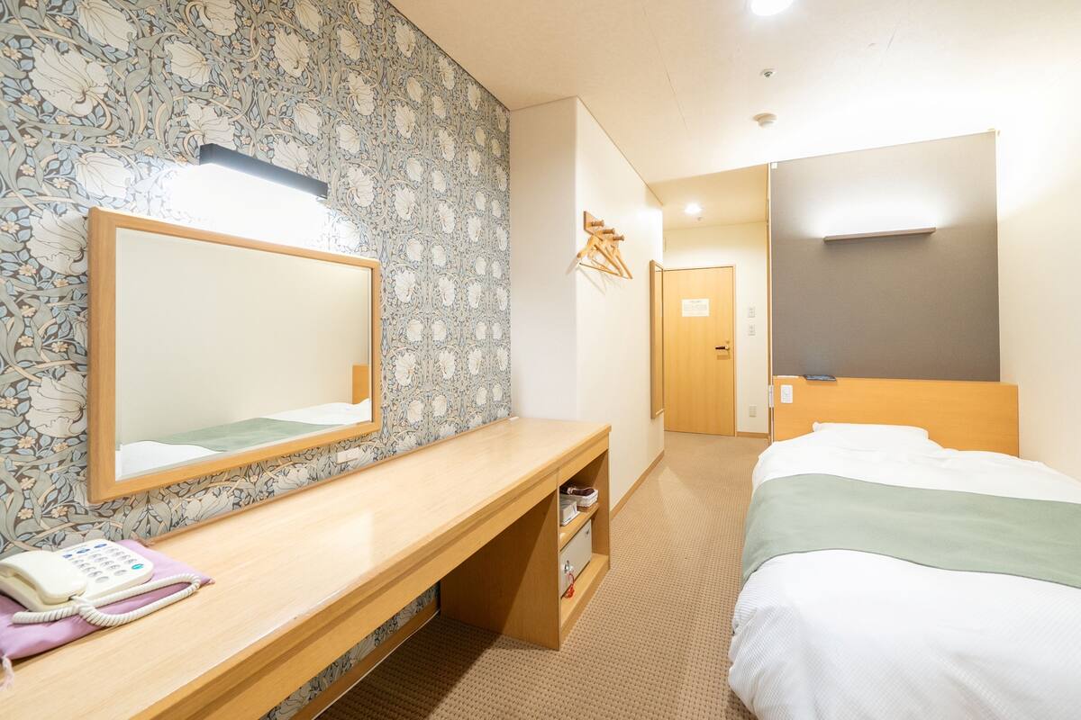 Une chambre d’hôtel avec un bureau en bois, un téléphone, un miroir, un lit et une armoire.
