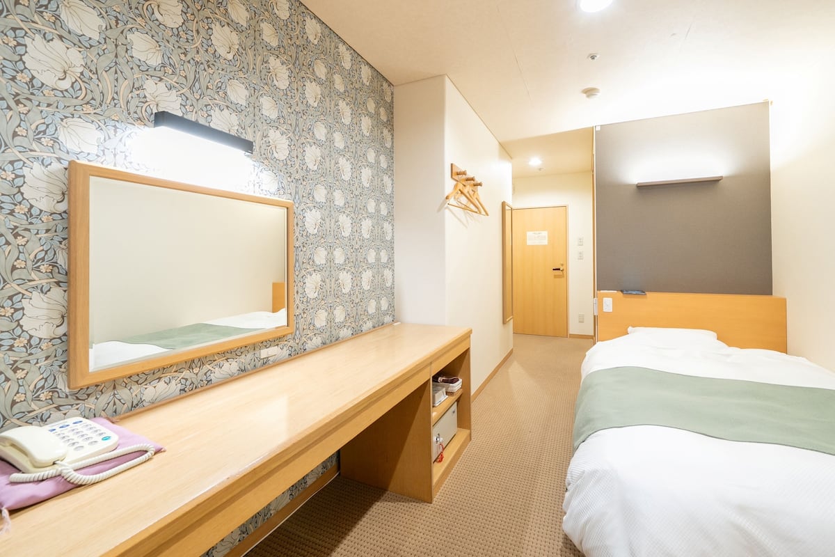 Una habitación de hotel con un escritorio de madera, un teléfono, un espejo, una cama y un armario.