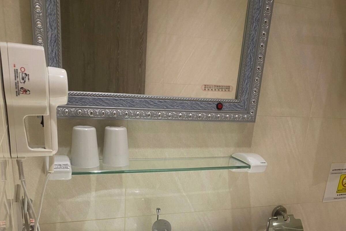 Kylpyhuoneessa on valkoinen pesuallas, peili ja wc-istuin. Seinällä on kuppeja ja saippua-annostelija.