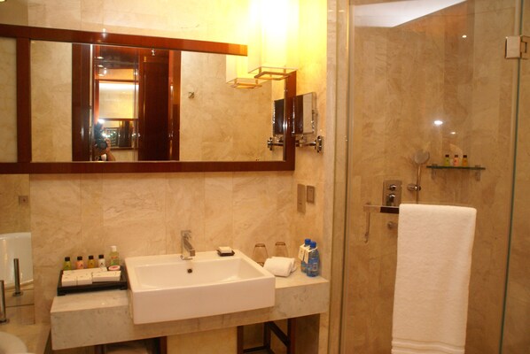 Un baño con un espejo grande, lavamanos, ducha y cabina de ducha con paredes de vidrio.