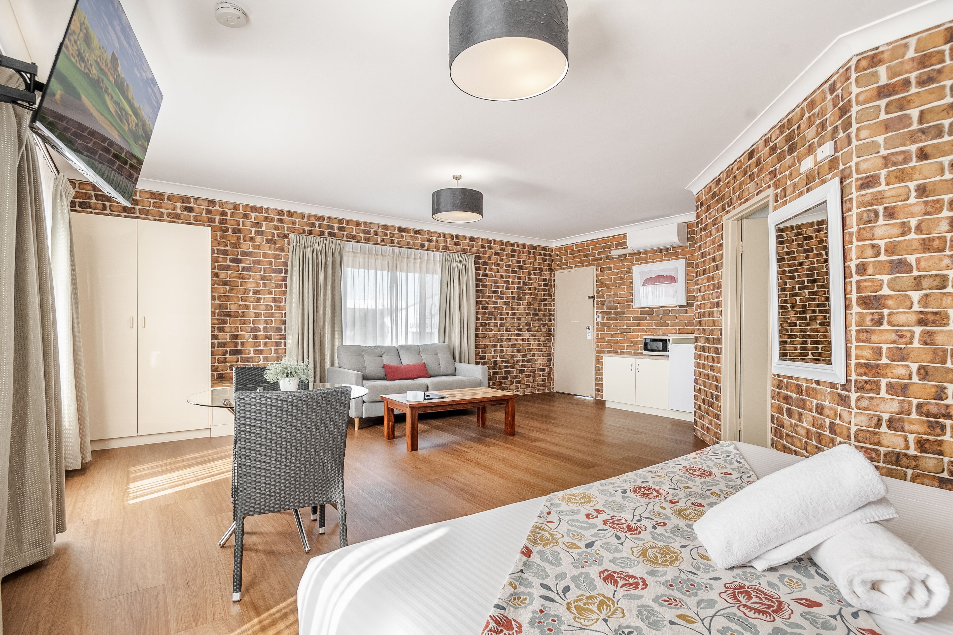 Een hotelkamer met een bakstenen muur, een bed met bloemenbedrukking, een bank, een bijzettafeltje en een aan de muur bevestigde televisie.