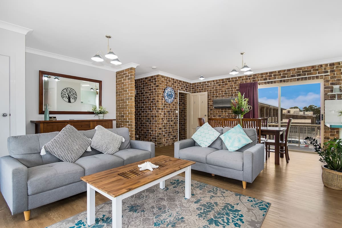 A modern living room with two grey sofas, a wooden coffee table, and a brick accent wall.