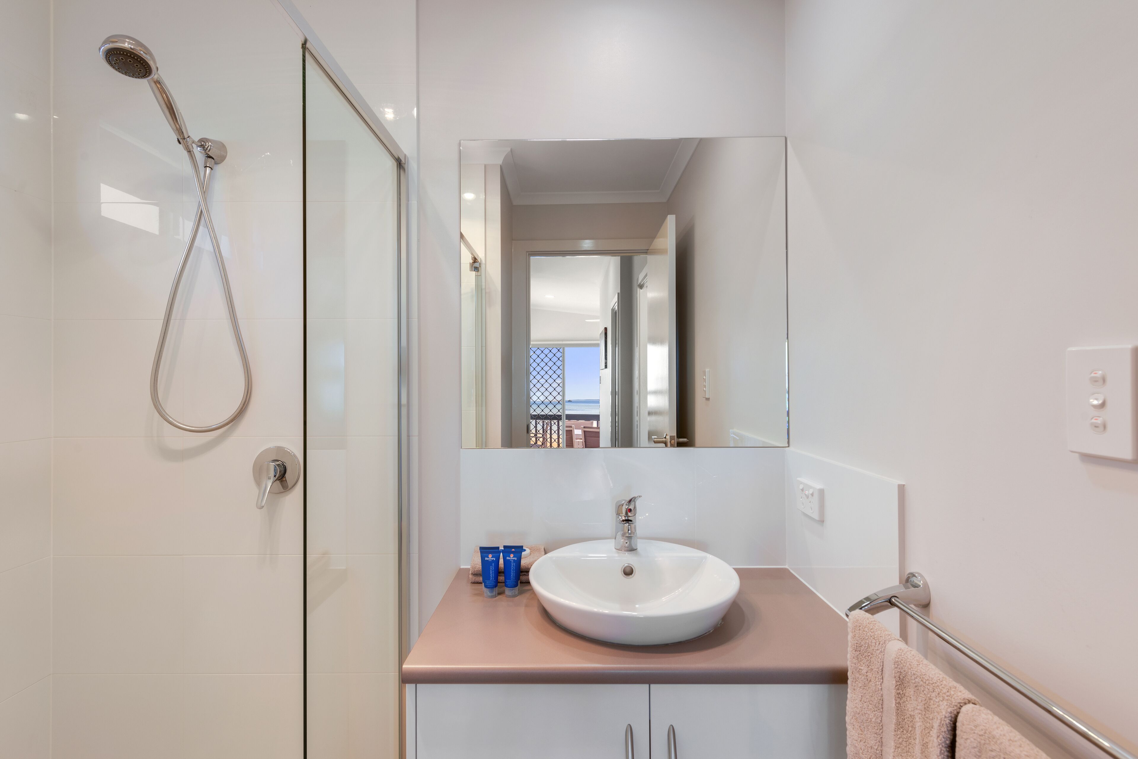 A modern bathroom with a glass shower enclosure, a white sink, and a mirror above it.