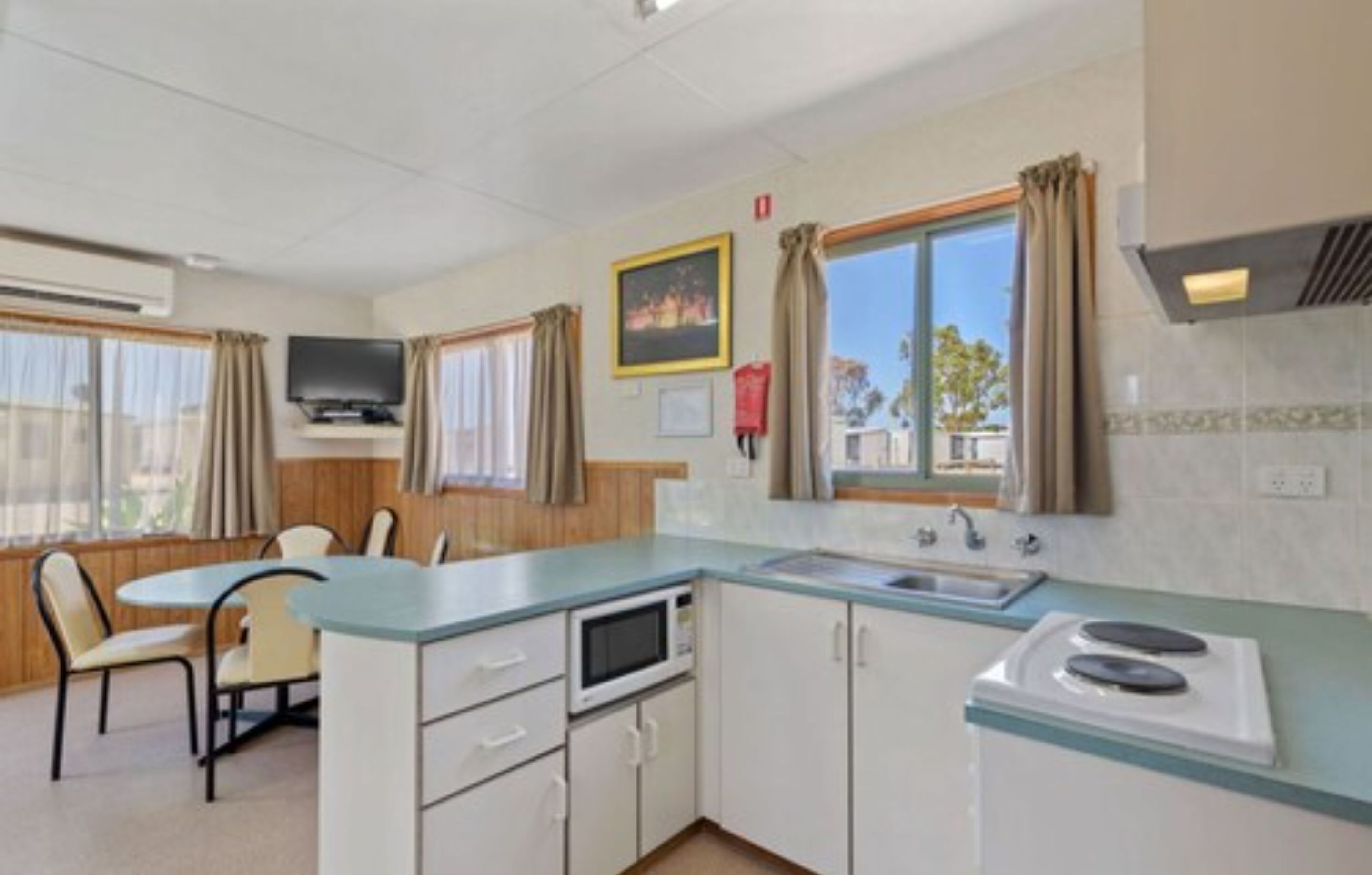 A compact kitchen with a microwave, stove, and sink. There is a dining area with chairs and a table.