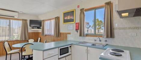 A compact kitchen with a microwave, stove, and sink. There is a dining area with chairs and a table.