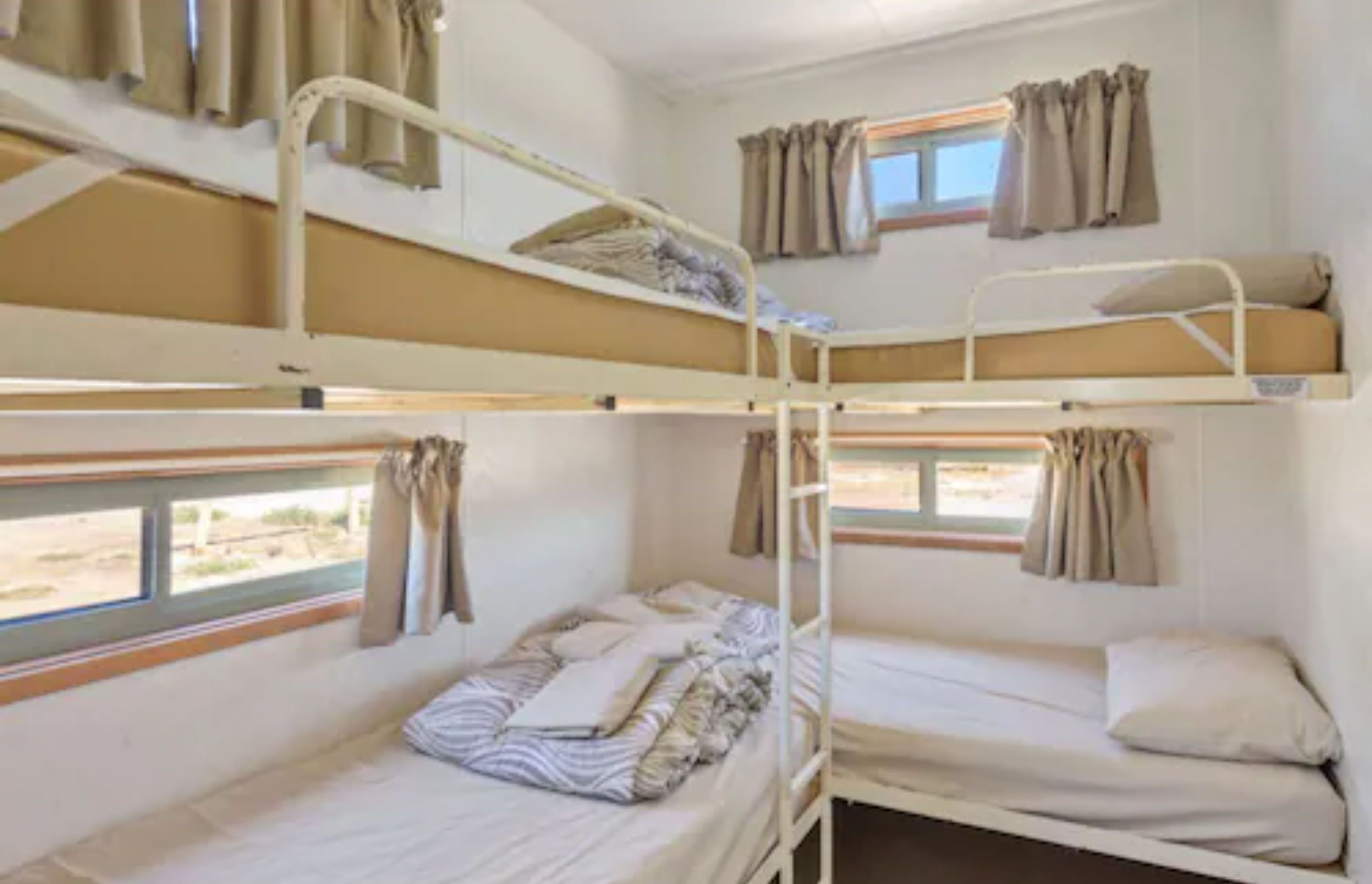 A bunk bed room with two windows, curtains, and a view of the outside.