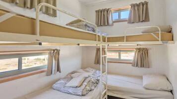 A bunk bed room with two windows, curtains, and a view of the outside.