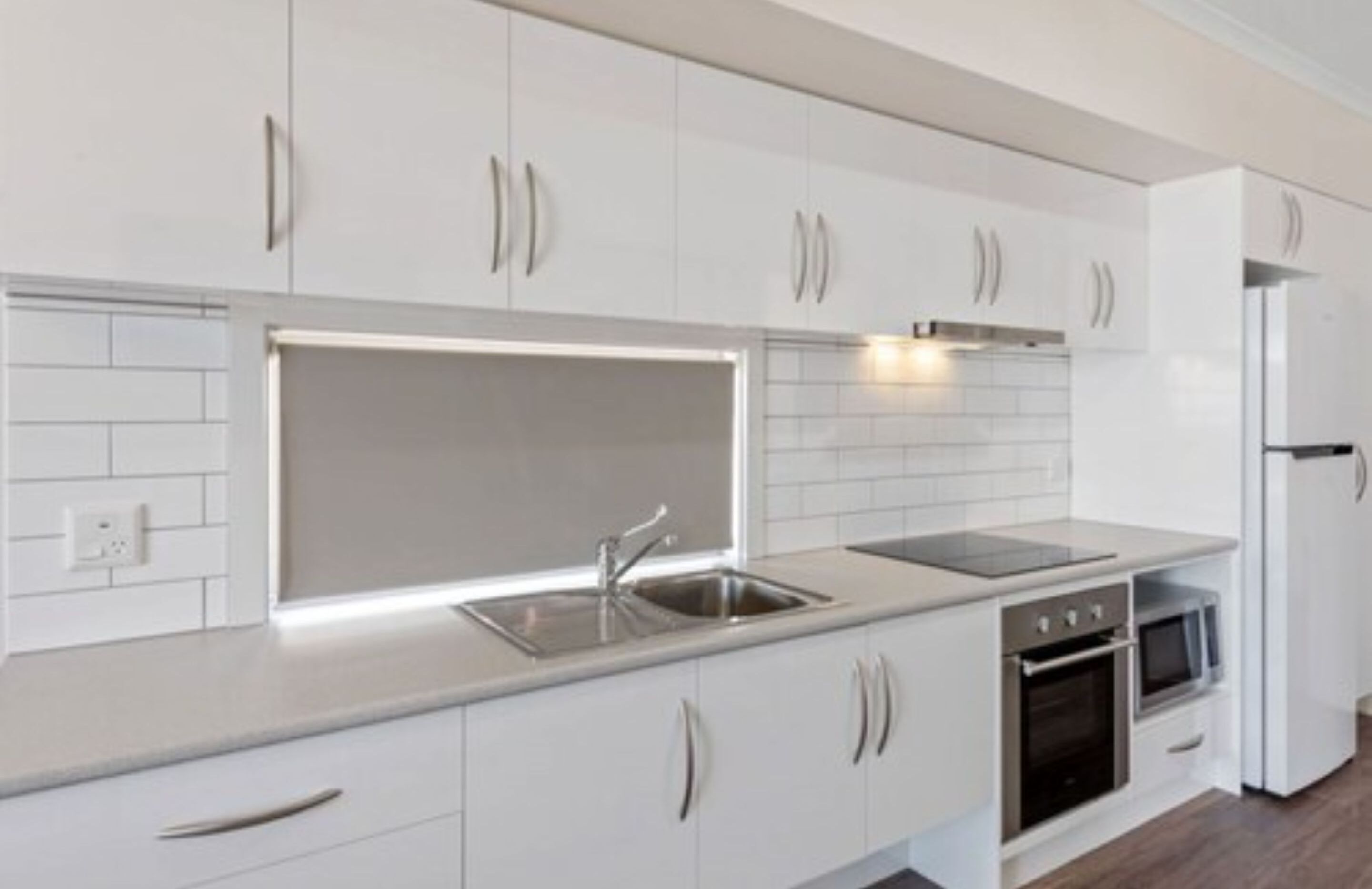 A modern kitchen with white cabinetry, a stainless steel sink, a built-in oven, and a microwave.