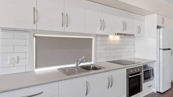 A modern kitchen with white cabinetry, a stainless steel sink, a built-in oven, and a microwave.