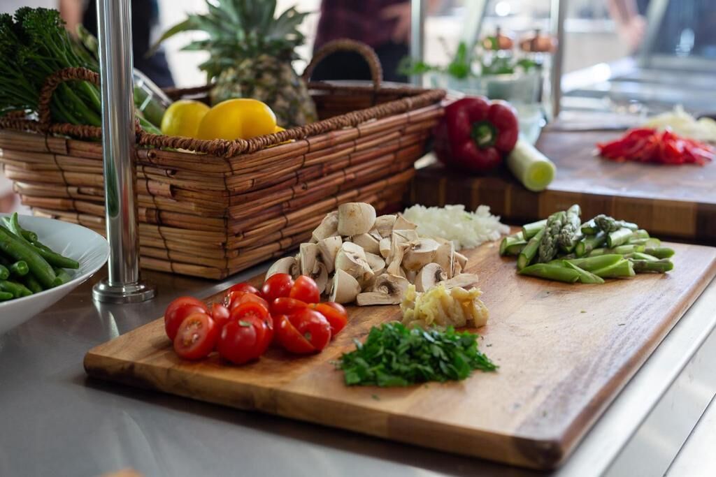 Una tabla de madera con varios vegetales y una cesta de productos frescos.