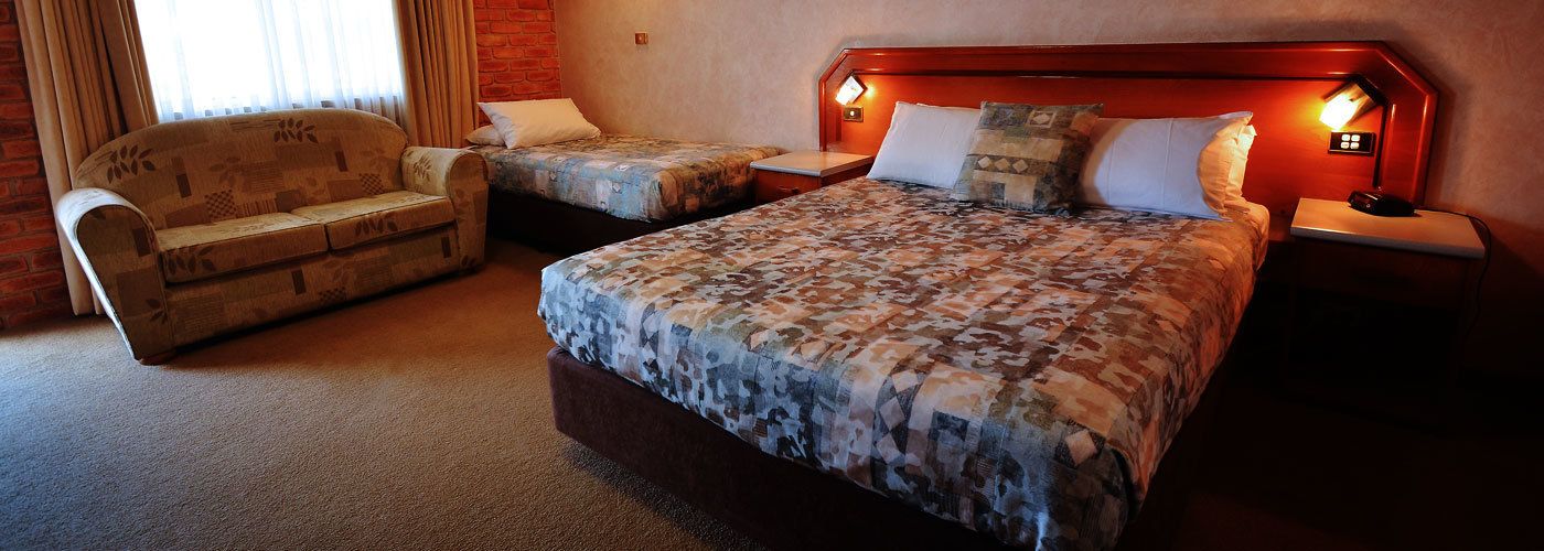 A hotel room with a large bed, a sofa, two bedside tables, and a brick wall.