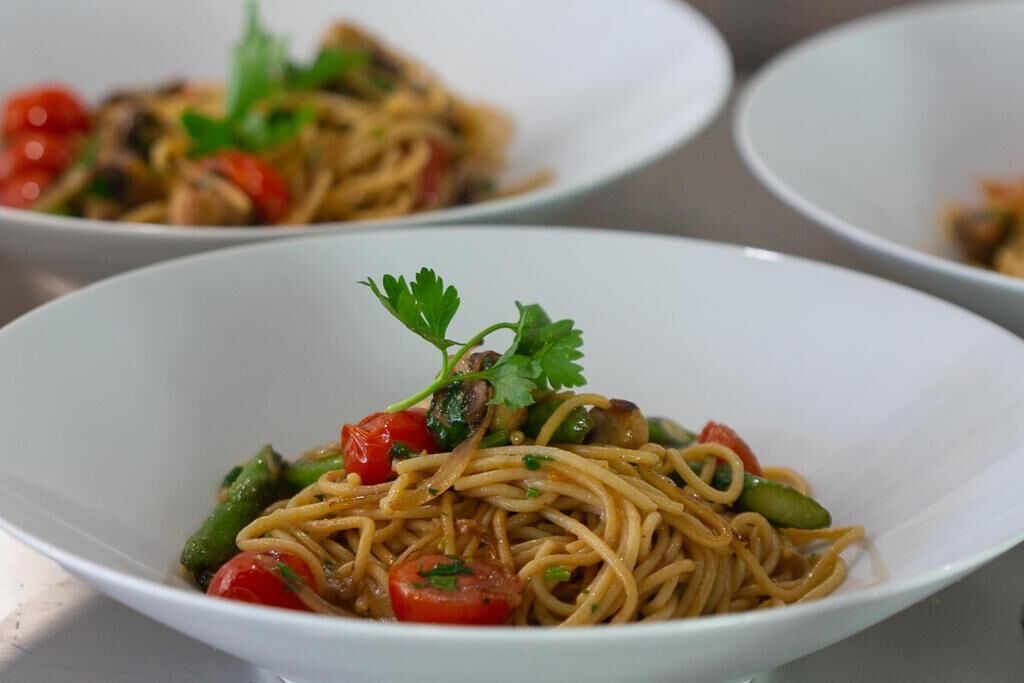 A bowl of noodles with vegetables and a garnish.