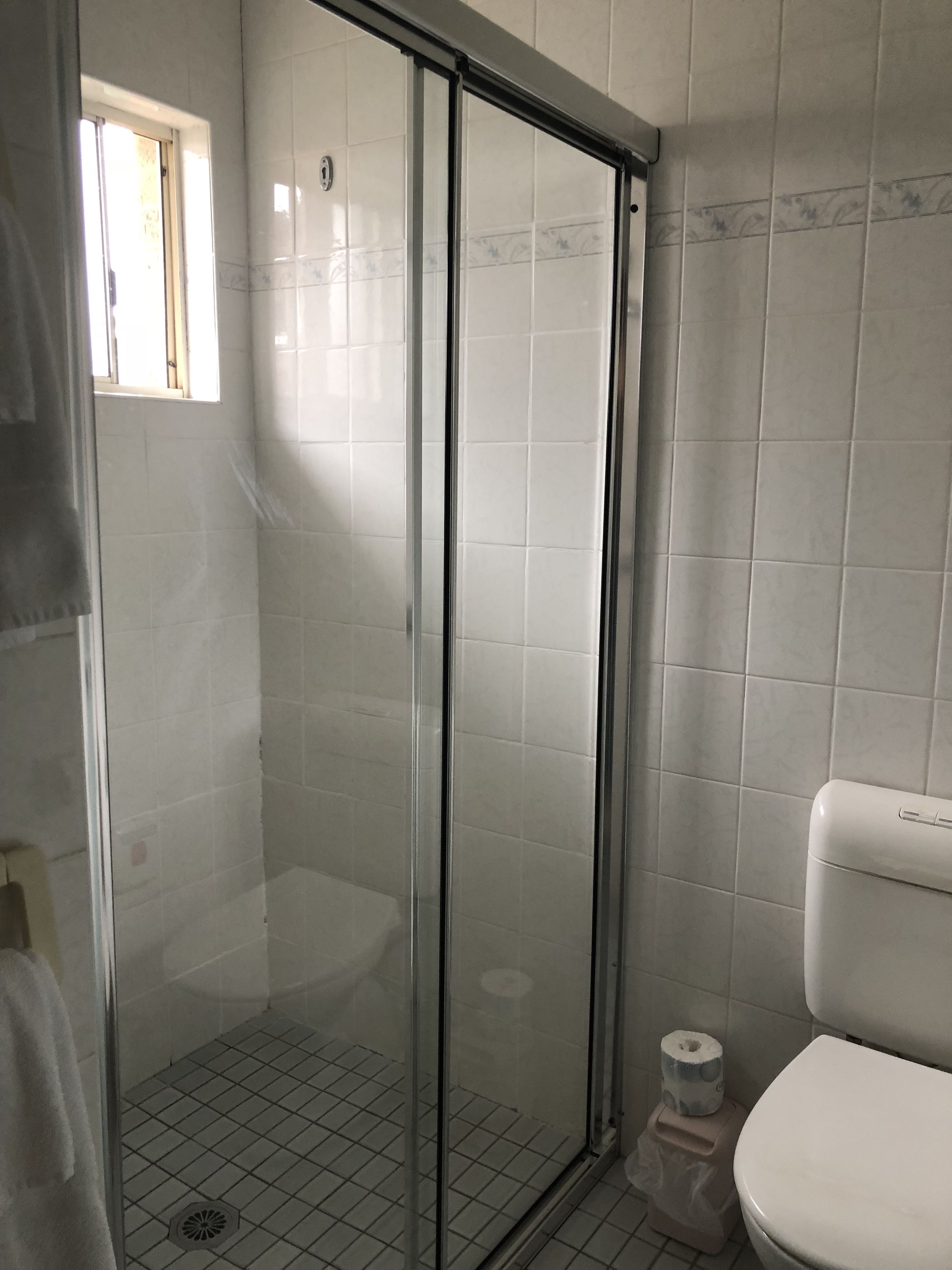 A bathroom with a glass shower enclosure, a toilet, and a window.