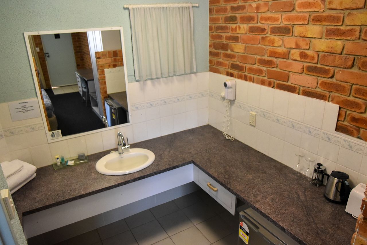 A bathroom with a sink, mirror, towel rack, and a brick wall.