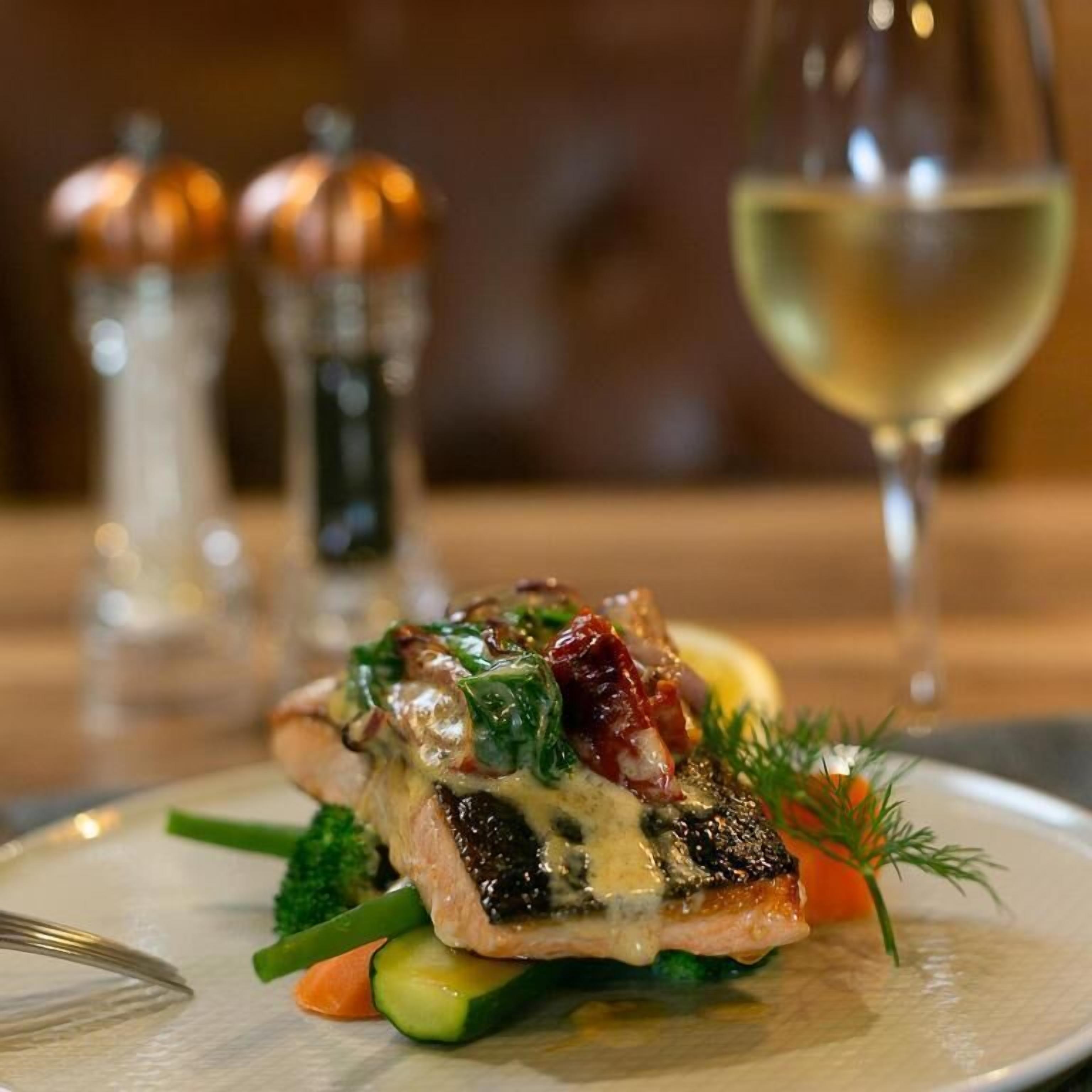 A plate of food with a fish fillet, vegetables, and a glass of white wine.