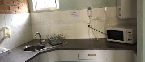 A kitchen with a sink, a microwave, a dish rack, and a trash bin.