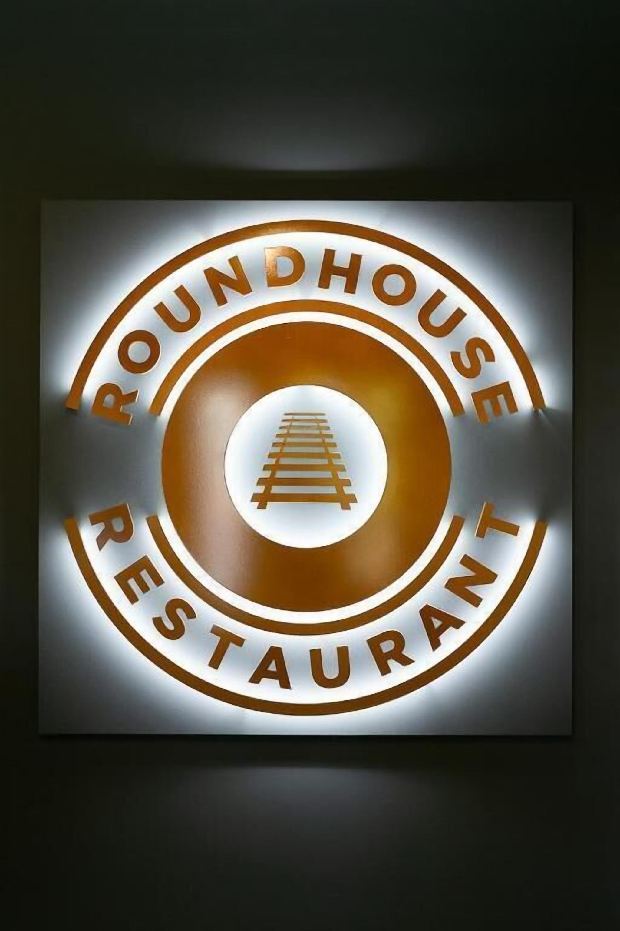 Une enseigne pour le restaurant Roundhouse, de forme circulaire, avec une image centrale représentant un train.