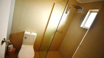 Une salle de bain avec des toilettes, une douche à parois de verre et une petite fenêtre.