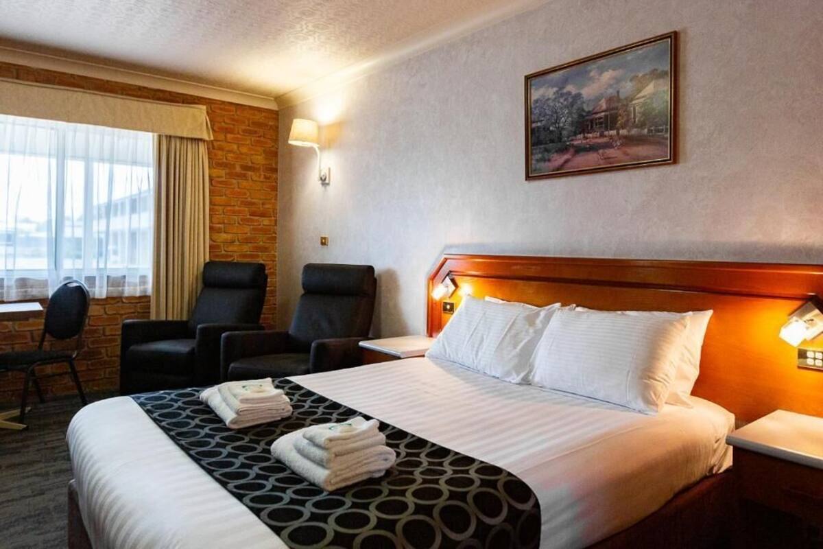A hotel room with a bed, two chairs, a desk, and a painting on the wall.