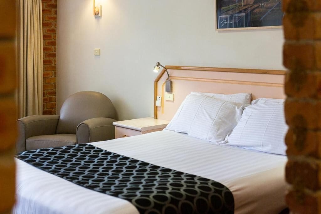 A hotel room with a bed, a chair, a nightstand, and a lamp.