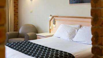 A hotel room with a bed, a chair, a nightstand, and a lamp.