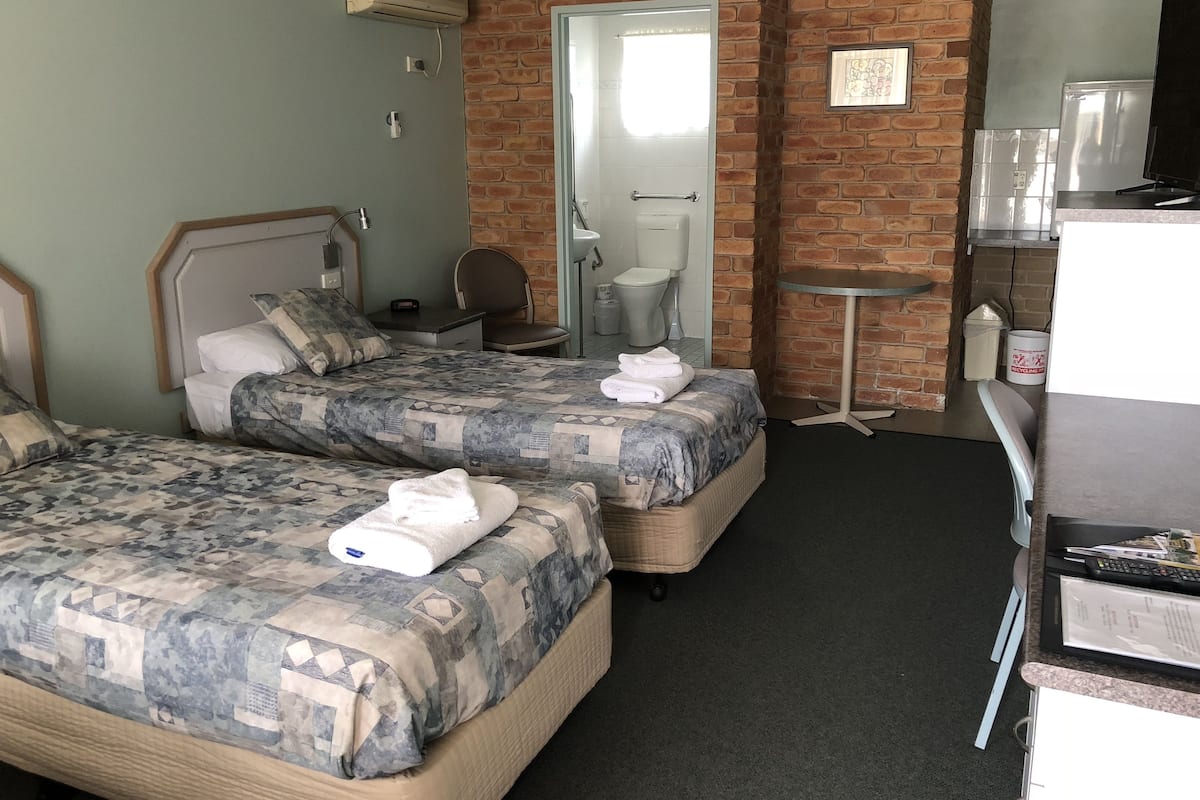 A hotel room with two beds, a small desk, a chair, a TV, and a refrigerator.