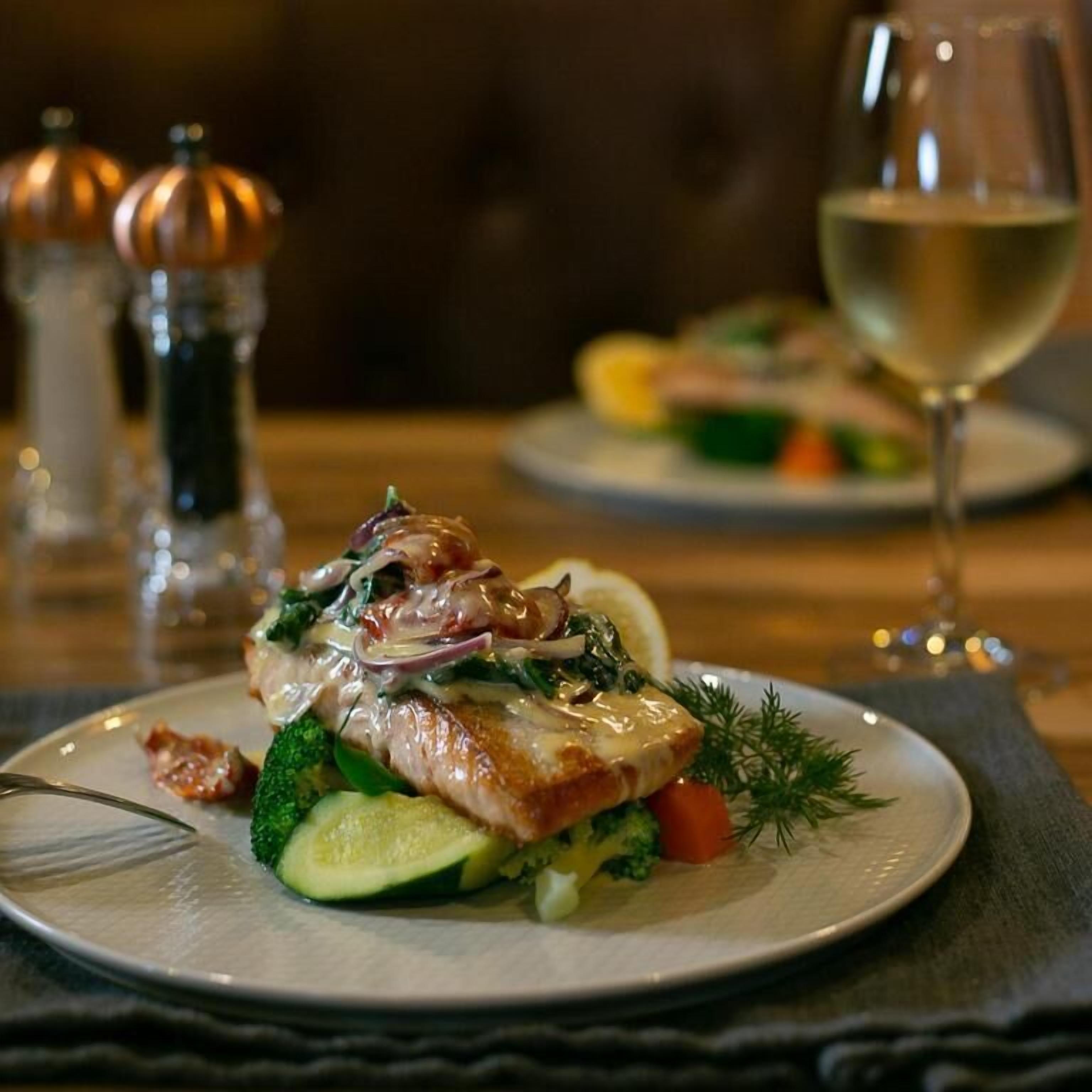 A plate of food with vegetables and a glass of white wine on a table.